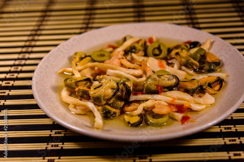 Ceramic plate with different sea food and olives on a bamboo mat