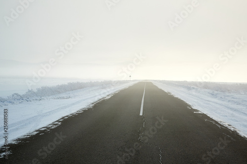 view of empty road with snow covered landscape while snowing in winter season. © Oleg Picolli