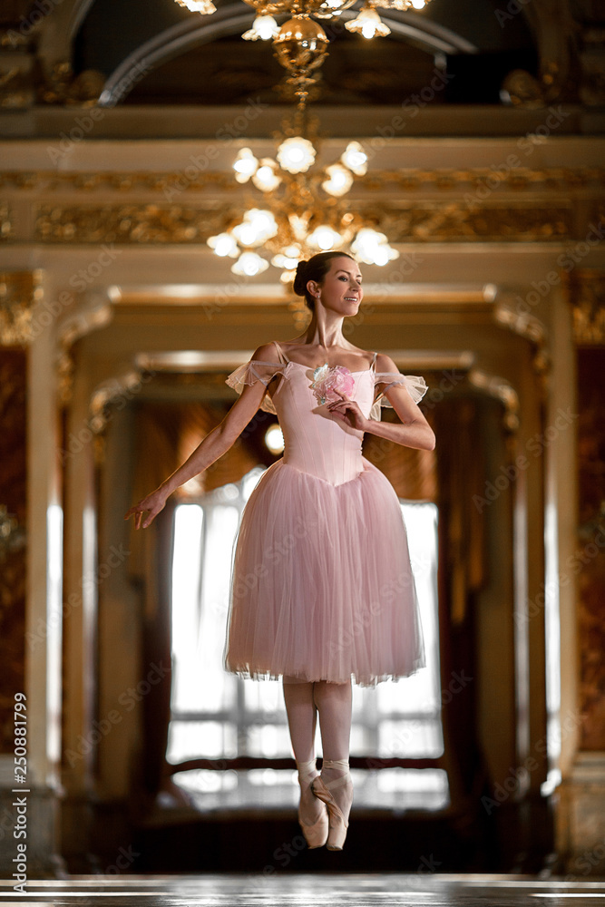 Beautiful ballerina dancing and jumping in a luxurious hall in a pink dress.