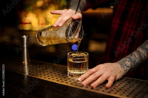 Bartender pouring a Rusty Nail cocktail from the measuring cup