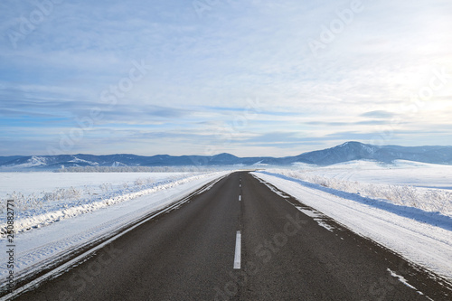 scenic view of empty road with snow covered landscape while snowing in winter season. Blue sky On the horizon.