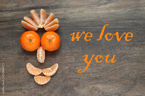composition of peeled and unpeeled mandarins in the form of a stylized face with a smile on the background of a wooden board   with an inscription "we love you"
