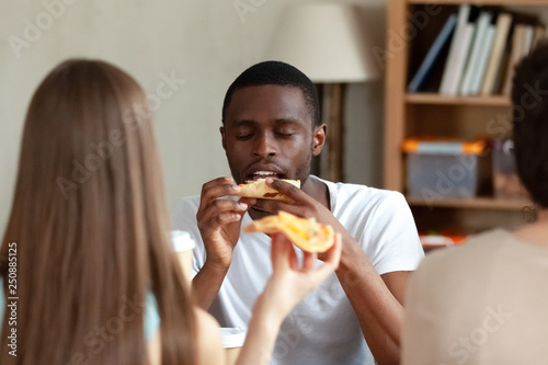 Happy African American man enjoying pizza with friends