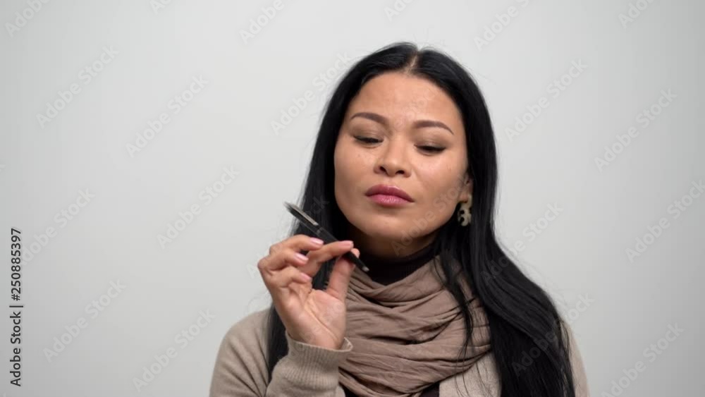 Pensive Asian Woman with Narrow Eyes in a Beige Sweater on a White Background. Pensive Asian Woman with Narrow Eyes in a Beige Sweater on a White Background.