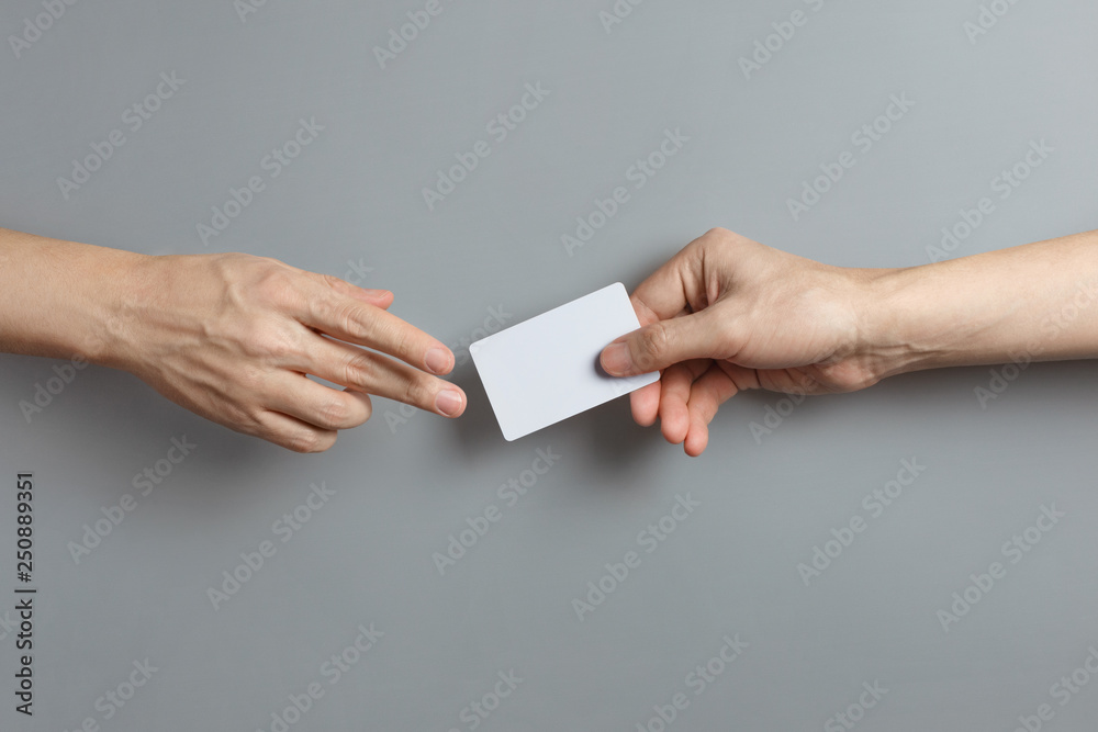Hands sharing a blank card or a ticket/flyer on gray background - obrazy, fototapety, plakaty 