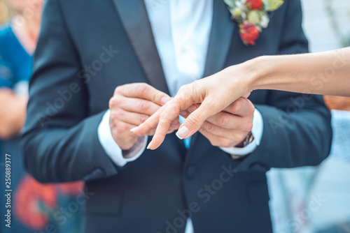 Groom In a dark blue jacket with a boutonniere puts a ring on the bride's hand. close-up shot of chest cropping photo