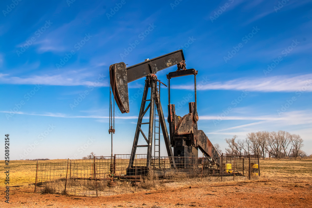 Large old rusty oil well pump jack surrounded by cattle panel fence out in field with very blue sky in winter. Large old rusty oil well pump jack surrounded by cattle panel fence out in field with very blue sky in winter.