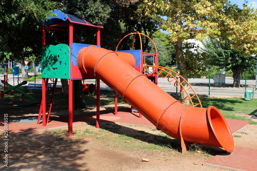 Large multifunctional colorful outdoor public playground equipment with plastic tunnel slide next to climbing pipes and stairs all connected with closed tunnel on local playground surrounded with gras