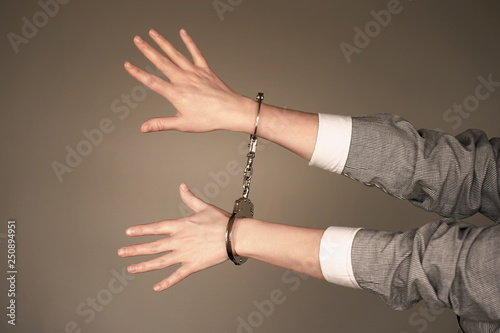 Arrested woman handcuffed hands. Prisoner or arrested terrorist, close-up of hands in handcuffs isolated on brown background. Criminal female hands locked in handcuffs. Toning