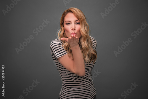Portrait of pretty blonde woman blowing air kiss on grey background. © Denis Rozhnovsky