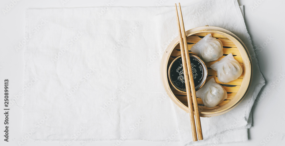 Traditional chinese steamed dumplings Dim Sums in bamboo steamer with sauces and chopsticks on light surface with copy space. Asian food background. Traditional chinese steamed dumplings Dim Sums in bamboo steamer with sauces and chopsticks on light surface with copy space. Asian food background.