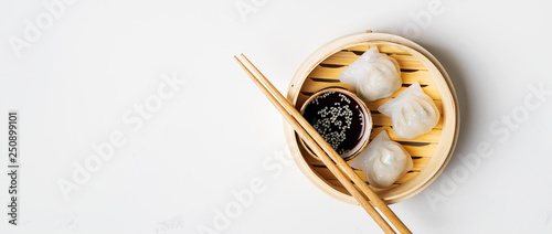 Traditional chinese steamed dumplings Dim Sums in bamboo steamer with sauces and chopsticks on light surface with copy space. Asian food background.