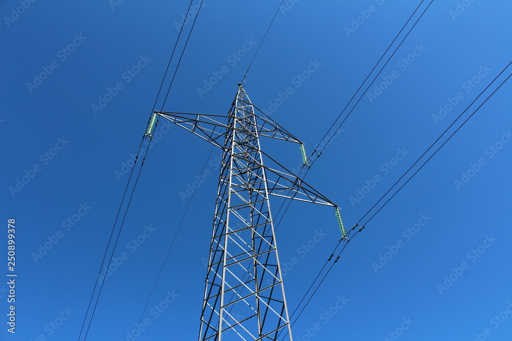 Mighty tall power line utility pole made of strong metal pipes with multiple electrical wires connected with glass insulators on clear blue sky background on warm sunny day