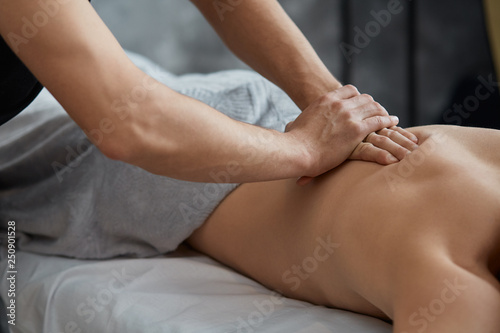 Young handsome man enjoying a back massage. Professional massage therapist is treating a male patient in apartment. Relaxation, beauty, body and face treatment concept. Home massage. photo