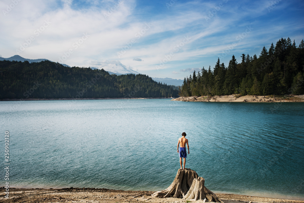 Teenage boy standing on tree stump on lake beach Teenage boy standing on tree stump on lake beach