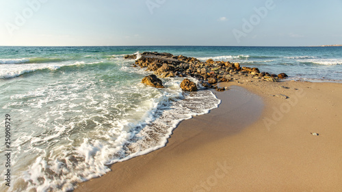 Afternoon sun shines on wild beach, some small waves hitting little rocks in background, empty clean sand spot (space for text) on right side. © Lubo Ivanko