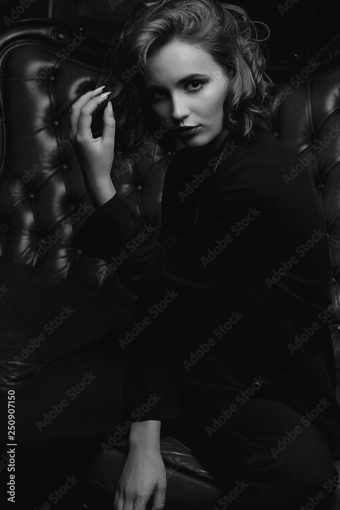Lovely young model with long hair wearing jacket posing on a vintage sofa. Black and white toning Lovely young model with long hair wearing jacket posing on a vintage sofa. Black and white toning