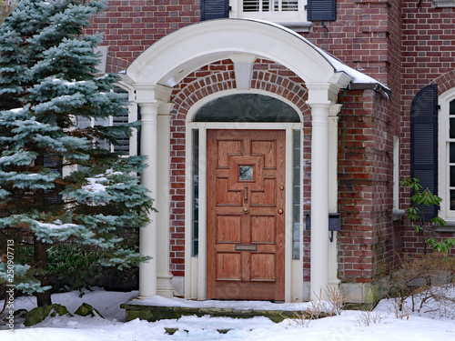 portico entrance of brick house with elegant wooden door and pine tree in winter
