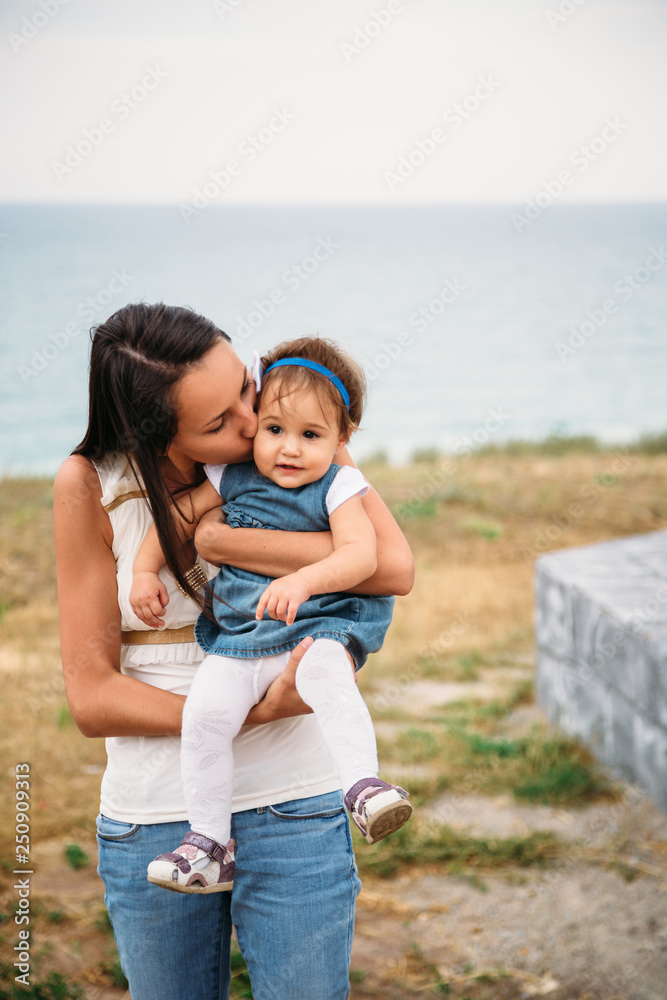 Happy young mother with a small daughter in hands hugging near to the lighthouse, outdoors background