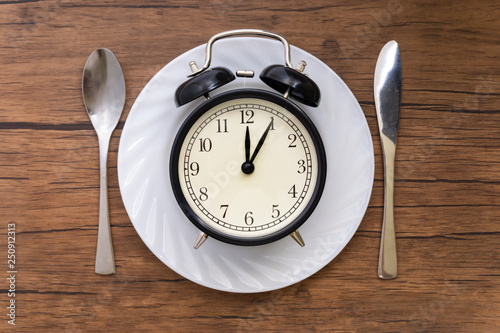 Alarm clock with spoon and knife on the table. Time to eat