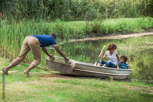 Mid-adult man pushing rowboat into river children (2-3, 14-15) watching 