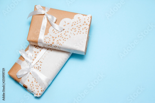 Gifts of craft paper decorated with a lace napkin on a blue background with copy space. Top view.