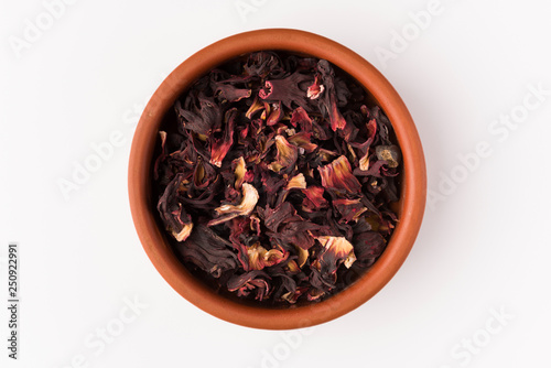 petals of dry hibiscus tea in the clay pot isolated on white background, top view
