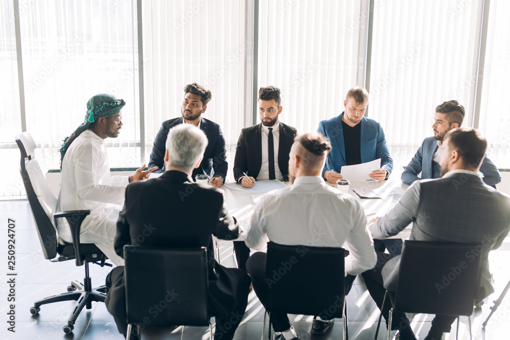 Focus group of advertising agency male stuff dressed in business suits sitting, headed by Executive dressed in arabian manner, interacting in Boardroom. Focus group of advertising agency male stuff dressed in business suits sitting, headed by Executive dressed in arabian manner, interacting in Boardroom.