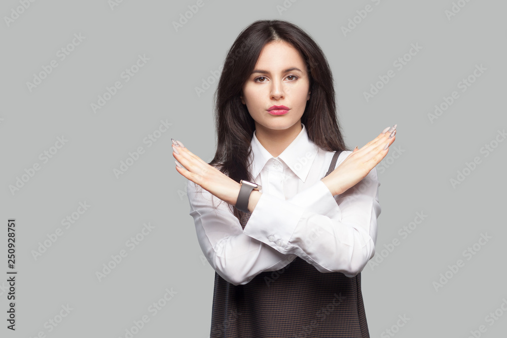 Portrait of serious beautiful young woman in white shirt and brown apron with makeup and brunette hair standing and showing X sign and looking at camera. studio shot, isolated on grey background. Portrait of serious beautiful young woman in white shirt and brown apron with makeup and brunette hair standing and showing X sign and looking at camera. studio shot, isolated on grey background.