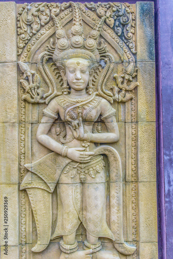 An Apsara dancing carved on the sandstone wall background. Apsara is a female spirit of the clouds and waters in Hindu culture. Her figure prominently in the sculpture, dance, literature and painting.