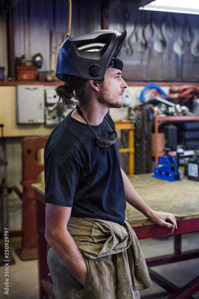 Side view of young mechanic wearing helmet standing in workshop Side view of young mechanic wearing helmet standing in workshop