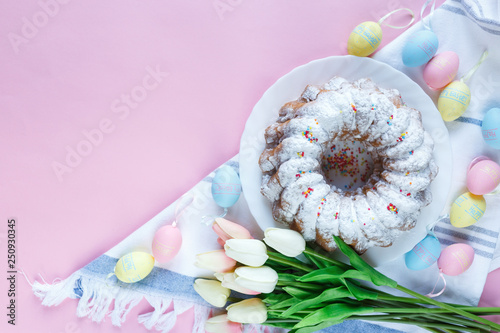 Happy Easter! Big plate with cake and hand painted colorful eggs, tulips and cup of coffee on pink background. Close up. Decoration for Easter, festive background.