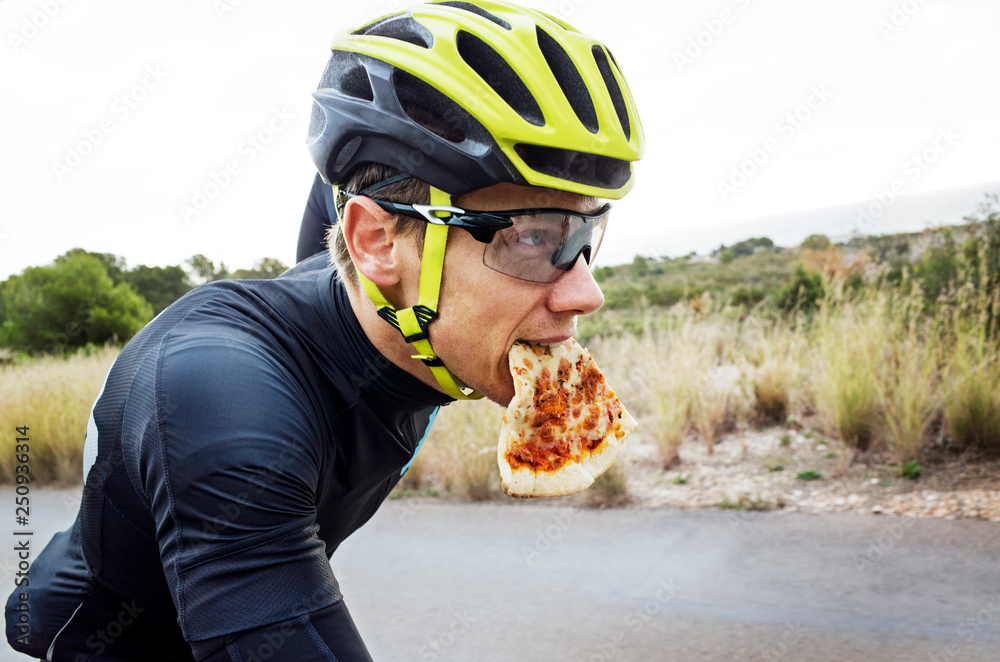 Cyclist holding slice of pizza in mouth 