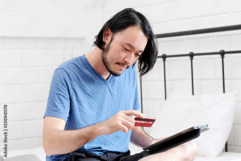 Young asian man holding credit card and using digital tablet for shopping on line at home, business and technology concept, digital marketing, casual lifestyle Young asian man holding credit card and using digital tablet for shopping on line at home, business and technology concept, digital marketing, casual lifestyle