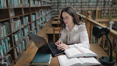 Young female student typing on laptop in library