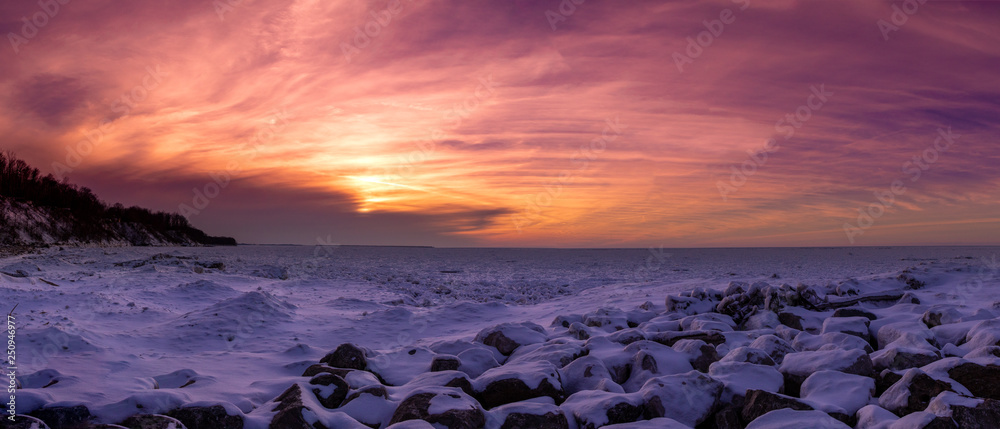Colorful winter sunset with ice and snow on the beach and rocks