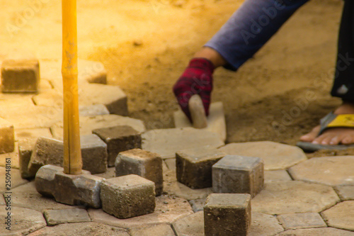 Construction workers are laying concrete pavement stone for footpath work at the construction site. Paving stone worker is putting down concrete pavement blocks during a construction of a city street.