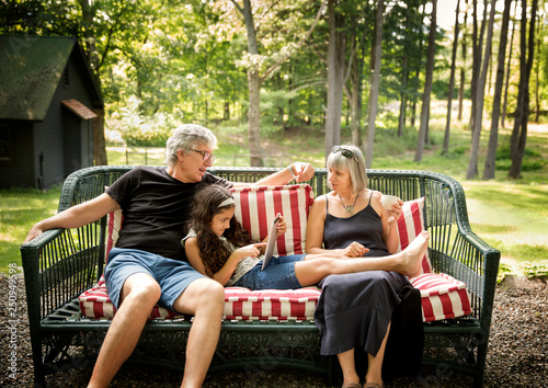 Grandparents sitting with granddaughter (8-9) on bench in backyard 