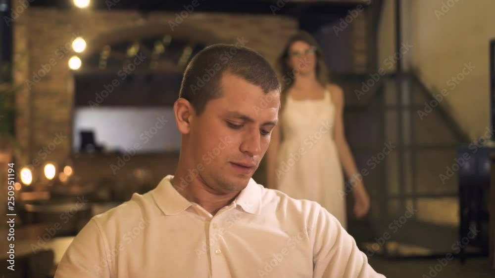 Young man waiting woman in evening restaurant for romantic dinner. Playful woman closing eyes boyfriend with hand at romantic date in elegant restaurant. Happy couple in evening cafe. Young man waiting woman in evening restaurant for romantic dinner. Playful woman closing eyes boyfriend with hand at romantic date in elegant restaurant. Happy couple in evening cafe.