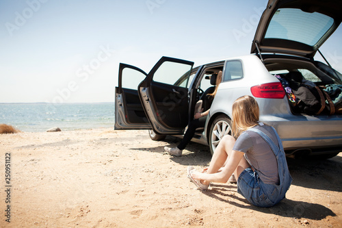 Young woman sitting next to car and tying shoes on beach  photo