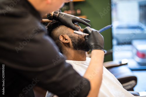 Skillful barber. Young bearded indian man getting an old-fashioned shave with straight razor