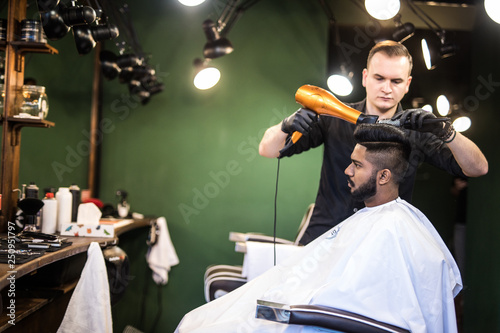 Looking good already. Close up side view of young bearded man getting groomed by hairdresser with hair dryer at barbershop