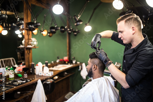 Handsome bearded man is smiling while having his hair cut by hairdresser at the barbershop. Hairdress concept.