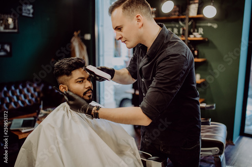 Professional hairdresser doing haircut man hair. Cutting electric razor. Beauty saloon. Male beauty. The client is a hipster.
