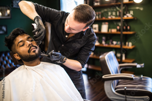 Close up. Young Man with beard client in barbershop hairdresser Barber on shaving electric razor