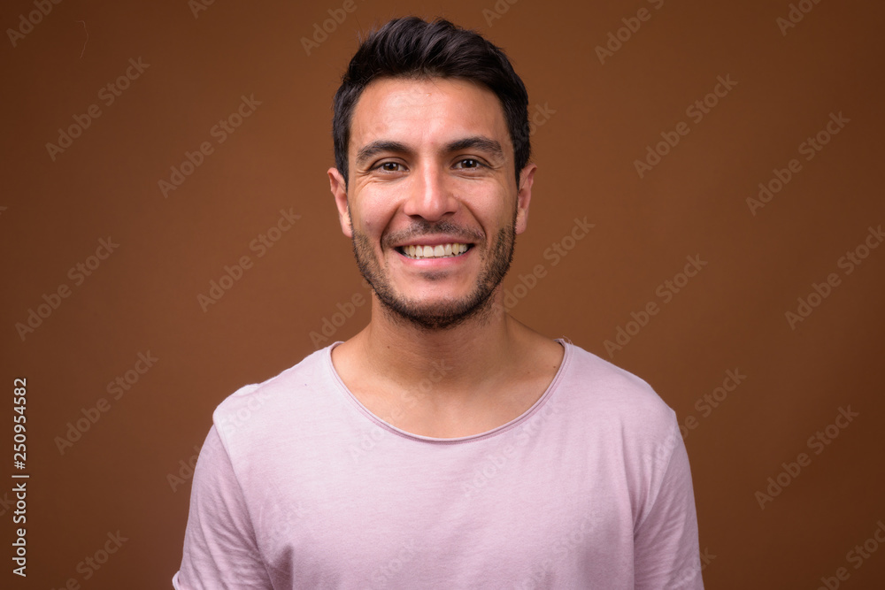 Obraz premium Young handsome Hispanic man smiling against brown background