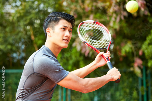 young asian man playing tennis outdoors