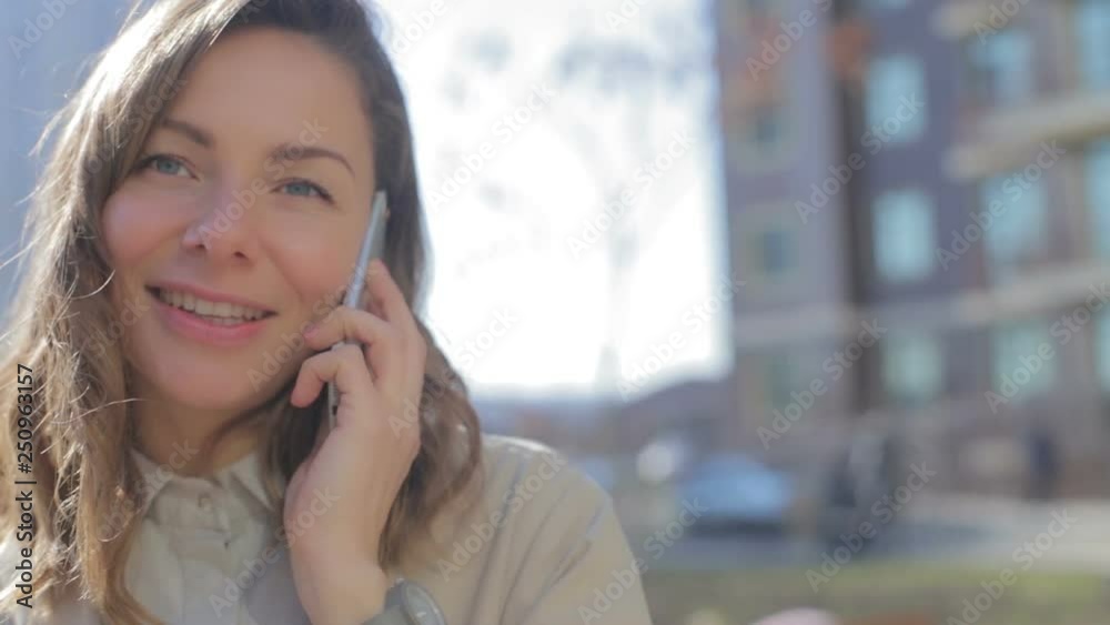 slow motion closeup attractive blonde long haired girl speaks on phone smiles against large building on bright sunny day slow motion closeup attractive blonde long haired girl speaks on phone smiles against large building on bright sunny day