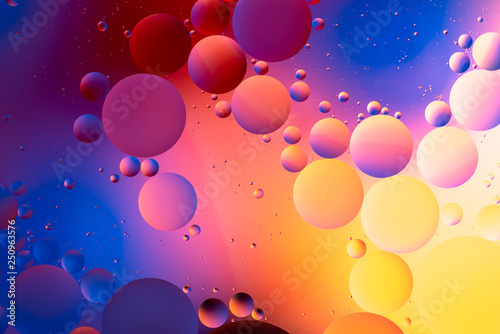 oily drops float into the water with a colorful background, closeup