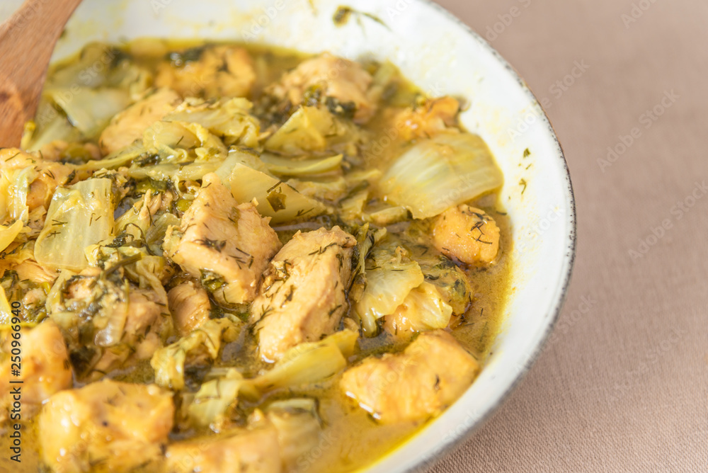 Chicken with Chinese cabbage in curry sauce in a bowl on a light background - a traditional Asian dish